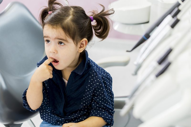 Little girl sits on a dentist chair pointing at one of her teeth