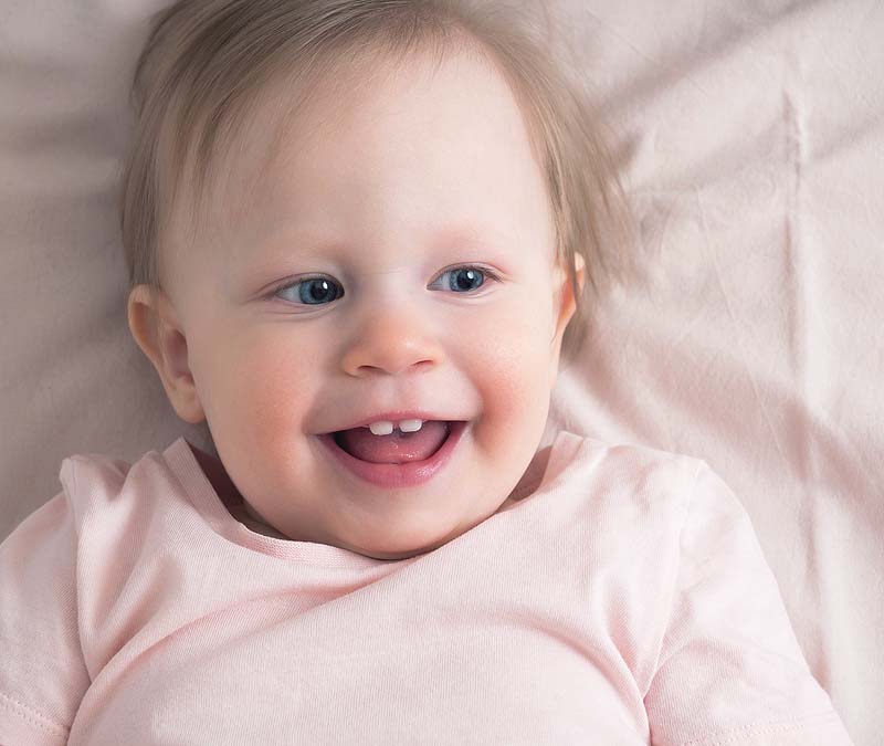 Smiling baby girl shows her first few teeth
