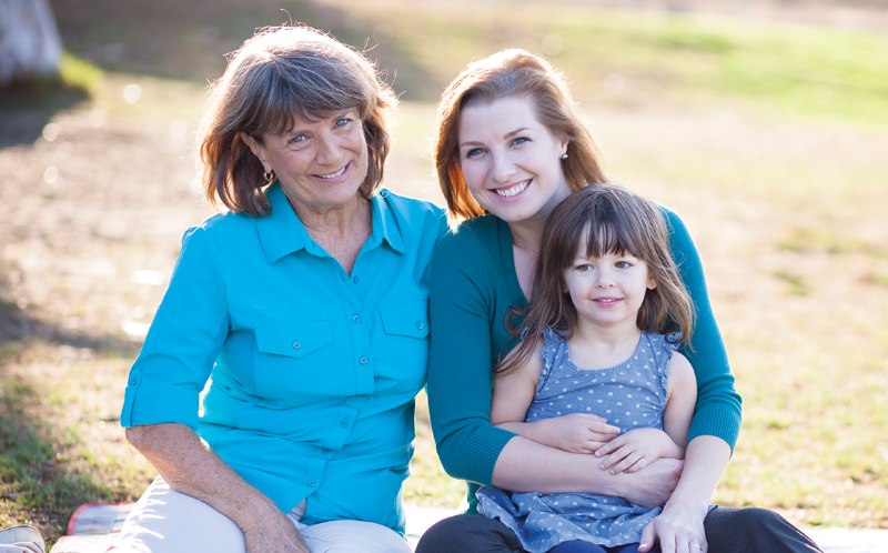 Mother holding her child with the grandmother seated next to them outdoors