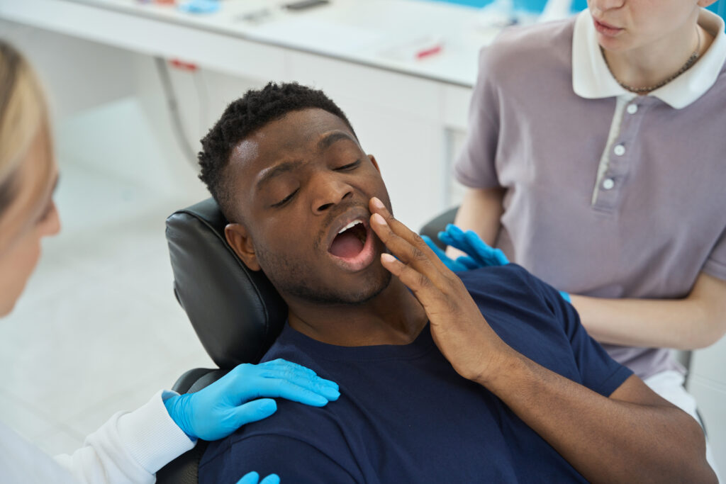 Young man holds his numb face on dentist chair