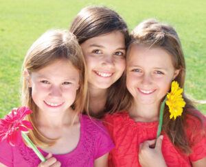 Three young girls smile outside holding picked flowers