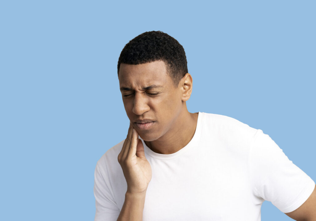 Man holds his cheek and squints in pain from toothache.